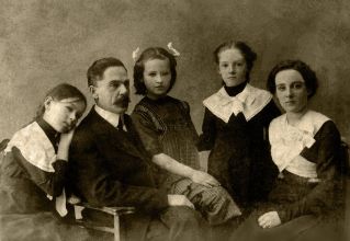 Vintage photo of calm mother and father sitting in studio with daughters in old fashioned clothes