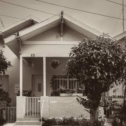 Early 1900s house with a gated porch; tree in front of the home.